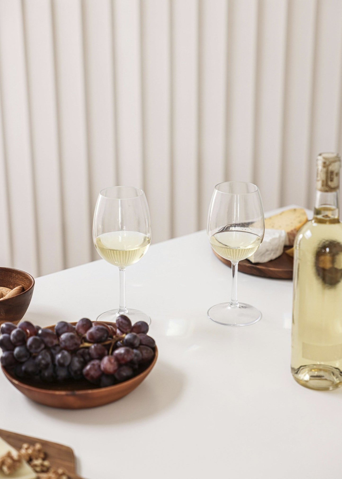 Tabletop scene with wine glasses, grapes, and cheese, evoking the fruity and vibrant scent profile of Grape Burst Room Spray for home fragrance lovers.