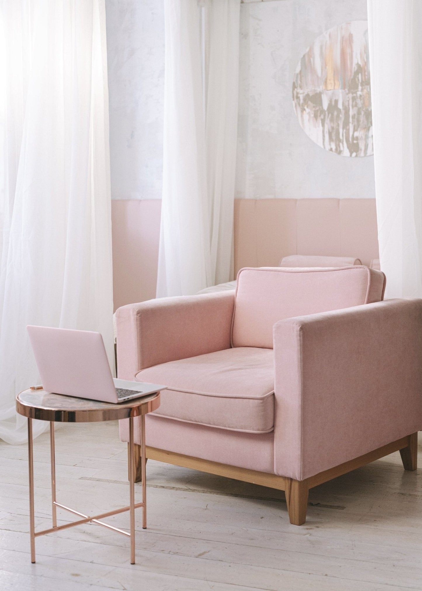 Cozy pink armchair and laptop on rose gold table in a soft-lit room, perfect setting for using Relax Room Spray - Florida Scents Essentials.