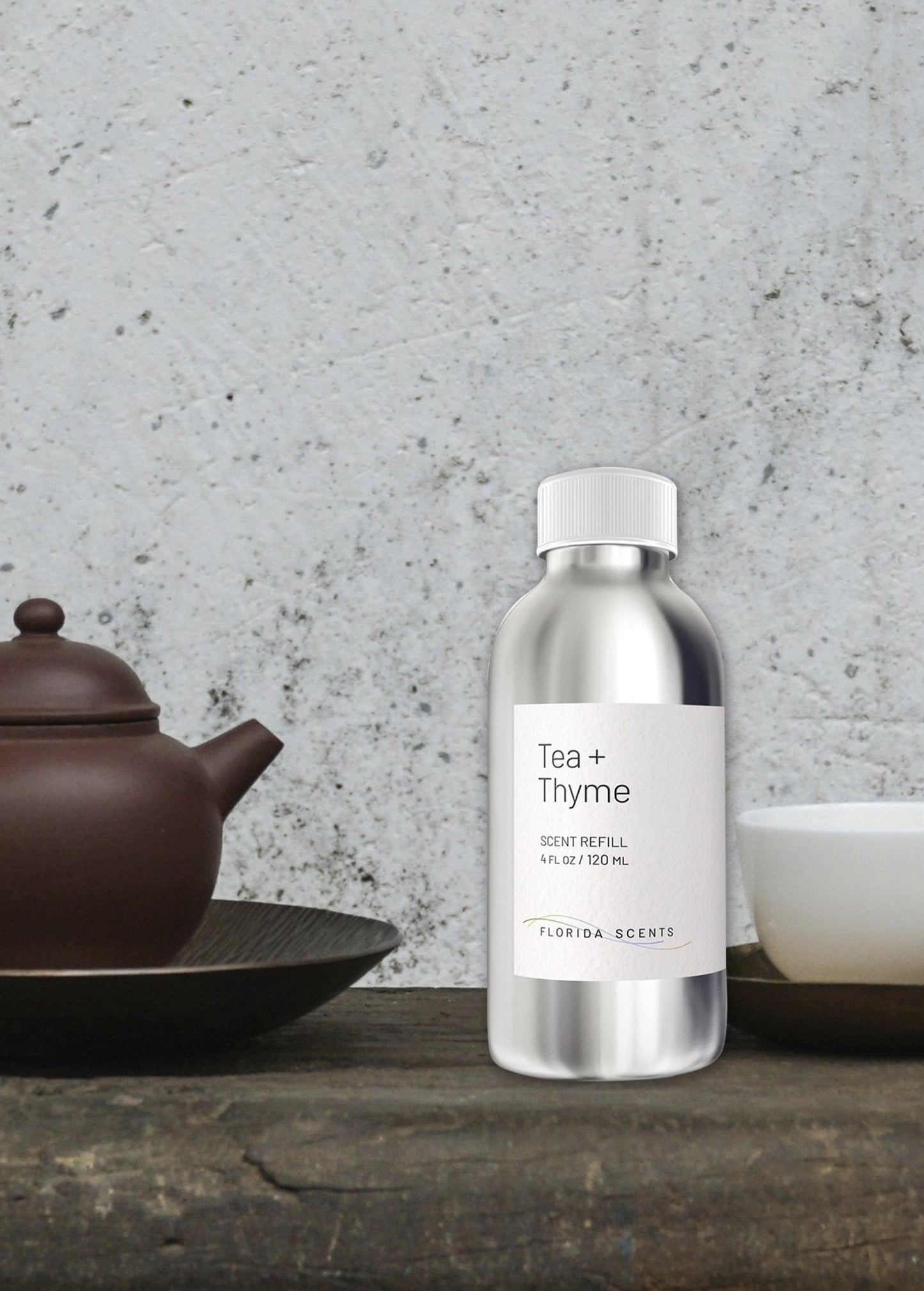Tea & Thyme Scent Refill by Florida Scents Essentials in a sleek silver bottle, placed beside a teapot and cup. Ideal for home fragrance relaxation.